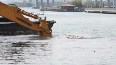 Mürettebatlı küçük bir tekne limanda yüzen çöpleri topluyor ve su temizleme çalışmalarına katkıda bulunuyor.