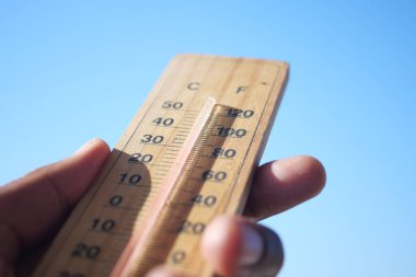 Bir el, açık mavi gökyüzüne karşı mevcut sıcaklığı gösteren bir termometre tutuyor.