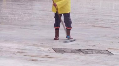 Parlak sarı güvenlik teçhizatlarıyla donanmış bir işçi süpürge kullanarak ıslak bir yüzeyi özenle temizler.