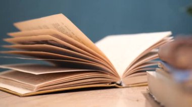 Yeşil bir arka plana karşı ahşap bir masa üzerinde sayfaları dönen açık bir kitap.