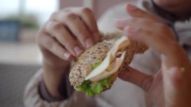 Marul ve hindi dilimleriyle bütün bir tahıllı sandviçi tutan ve yiyen kişiye yakın çekim..