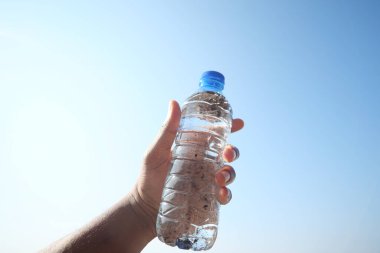 Mavi gökyüzüne karşı kirli su şişesi tutuyor. .