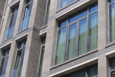 Binaların ön cephesi şehri yansıtan, mimariyi kentsel yaşamla harmanlayan geniş pencerelere sahiptir.