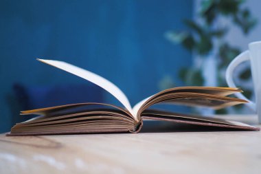 Yeşil bir arka plana karşı ahşap bir masa üzerinde sayfaları dönen açık bir kitap.