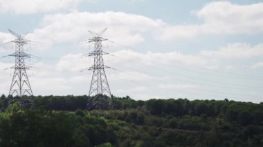 Parlak mavi gökyüzünün altındaki yeşil tepeler boyunca uzanan elektrik hatlarının manzarası.