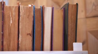 Ahşap bir kitaplık, içinde kitaplar, ahşap bir duvarın önünde portakal çiçeği vazosu.