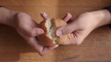 İki el nazikçe yeni pişmiş sıcak ekmeği kırsal bir ahşap masanın üzerinde kırıyor.