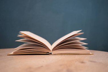 Yeşil bir arka plana karşı ahşap bir masa üzerinde sayfaları dönen açık bir kitap.