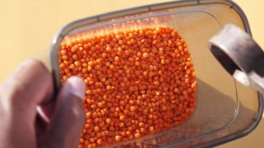 Bir el, parlak turuncu mercimeklerden oluşan bir kabı tutar ve zengin renklerini sergiler.