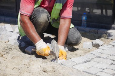 Becerikli bir işçi, güneşli bir açık havada, dikkatle ve ustalıkla kaldırım taşları yerleştiriyor.