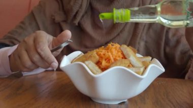 Sıcak bir restoranda taze ve sağlıklı bir salataya zeytinyağı döken bir insan, avokado ve ceviz sunar..