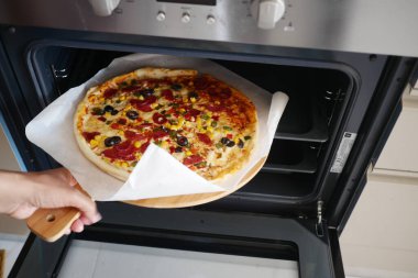 Person placing homemade pizza into oven with a safety glove, ready for baking. Enthusiastic cook. clipart