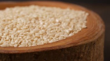 Kırsal ahşap bir kase ve kaşıkta beyaz susam tohumlarına yakın plan, arka planda kırmızı bir kumaş var..