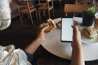 Kafede akıllı bir telefona bakarken lezzetli bir sandviçin tadını çıkarıyorum.
