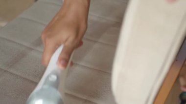 Bej bir kanepeyi vakumlayan, içeriyi temizleyen ve bakımını yapan birinin yakın çekimi.