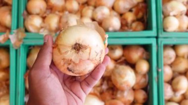 Kalabalık bir pazarın arka planında taze soğanları kucaklayan bir el.