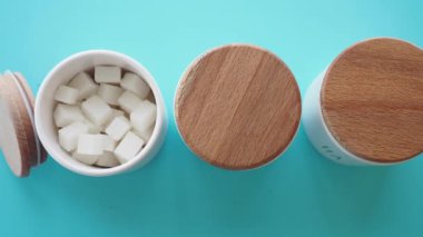 Canlı bir turkuaz yüzeye yerleştirilmiş şeker küpleriyle dolu modern kutular var.