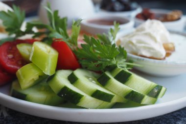 Dilimlenmiş renkli bir tabak salatalık, parlak domates ve aromatik otlar yemeği güçlendirir.