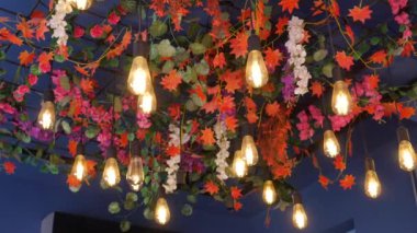 Renkli çiçeklerin ve zarif asılı ampullerin çarpıcı tavan görüntüsü izleyicileri cezbediyor.