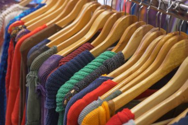 Canlı bir vitrin, ahşap askılara yerleştirilmiş çeşitli giysi parçalarını gösteriyor.