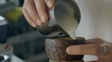 Yetenekli bir barista güzel oyulmuş dekoratif bir kaseye zengin, kremalı süt döker.