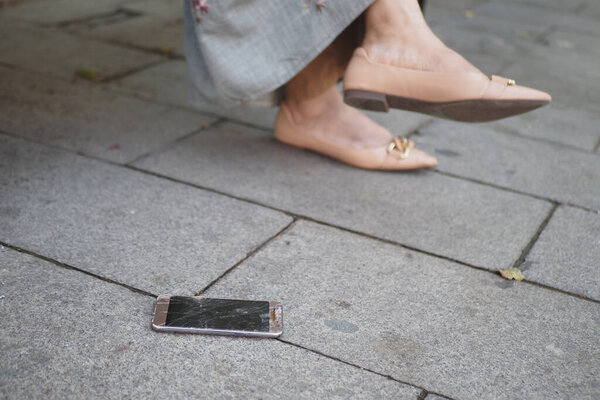 Смартфон лежит на бетонной площадке рядом с женскими модными ногами в стильной обуви