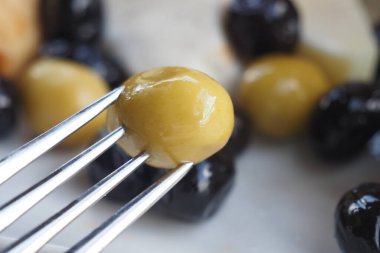 Bir çatalın üzerinde yeşil ve siyah zeytinlerin yakınlaşması, eşsiz dokularını ve renklerini vurgular.