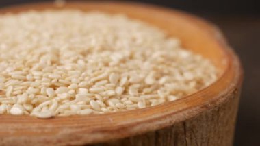 Kırsal ahşap bir kase ve kaşıkta beyaz susam tohumlarına yakın plan, arka planda kırmızı bir kumaş var..