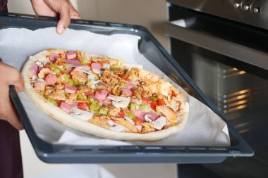 Ev yapımı pizzayı fırına koyan kişi emniyet eldiveniyle pişirmeye hazır. Hevesli aşçı.