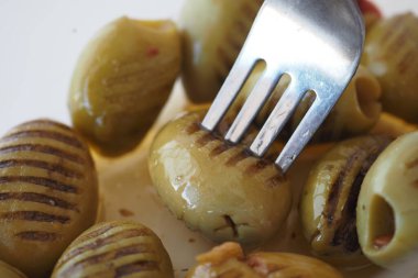 Lezzetli ızgara yeşil zeytin, bir çatalla sunulur, el değmemiş beyaz bir tabakta servis edilir.