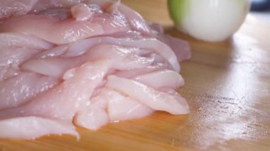 Çiğ tavuk göğsü filetoları tahta bir tahtada dilimlenmiş ve arka planda soğan var..