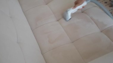 Bej bir kanepeyi vakumlayan, içeriyi temizleyen ve bakımını yapan birinin yakın çekimi.