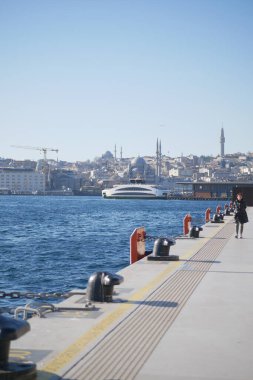 Sakin suların yanında modern yapıların yer aldığı huzurlu ve resimli bir rıhtım manzarası.