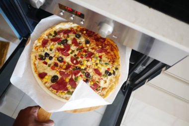 Ev yapımı pizzayı fırına koyan kişi emniyet eldiveniyle pişirmeye hazır. Hevesli aşçı.