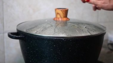 Mutfak sobasında cam kapakla kaplanmış, ahşap bir tokmağı olan siyah bir tencere..