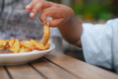 Küçük bir çocuk büyük bir hevesle dışarıdaki masaya yerleştirilmiş lezzetli kızarmış patateslere uzanıyor.