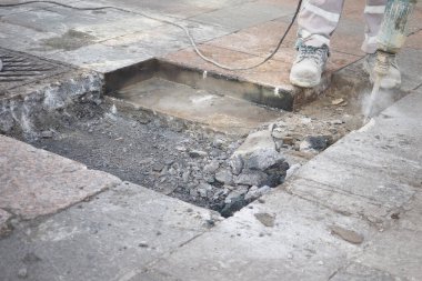 Bir kaldırım tamirhanesinde, bir inşaat işçisi ustalıkla güçlü bir kaya matkabını kullanır.