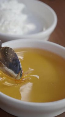 Arkaplanda kremalı ve pürüzsüz bir garnitür eşliğinde lezzetli bir kaşık dolusu bal.