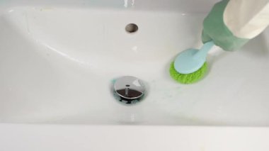 Bir el, etkili temizlik için tasarlanmış yeşil bir fırçayla temiz beyaz bir lavaboyu temizler.