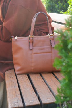 Zarif bir kahverengi çanta güzel bir şekilde açık hava ortamında bir bankın üzerine yerleştirilir.