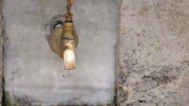 Yıpranmış dokulu bir duvara karşı yankılanan hafif bir damlaya sahip kırsal bir su musluğu.