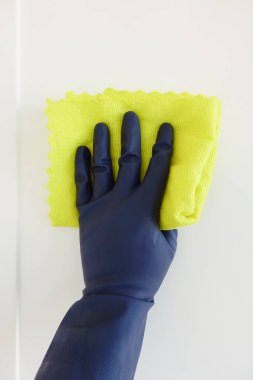 Mavi eldiven takan bir el, yumuşak sarı bir bezle bir yüzeyi özenle temizler.