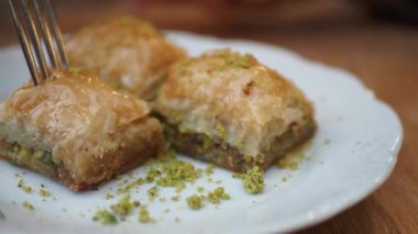 Taze yapılmış baklava, mükemmel bir şekilde ezilmiş fıstıkla kaplı, beyaz bir tabakta güzelce servis ediliyor.