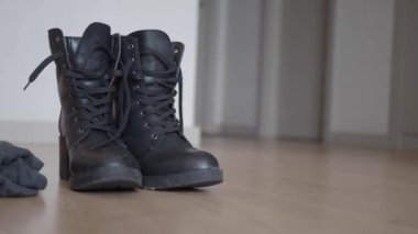 Ahşap bir zemine yerleştirilmiş şık bir çift siyah bot ve yakınlarda günlük giysiler.