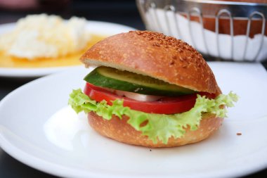 Kıtır salatalı, sulu domatesli ve tabakta taze salatalıklı renkli bir sebze burger.