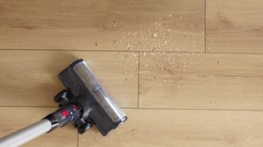 Elektrikli süpürge çeşitli enkazlarla dağılmış ahşap zemini etkin bir şekilde temizliyor.