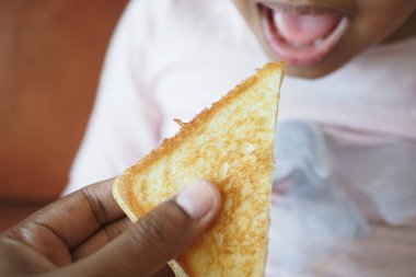 Bir el, neşeli bir çocuğa bir dilim peynirli tost ikram eder..