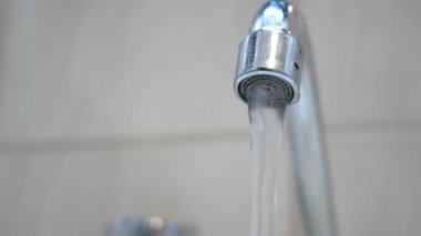 Temiz su zarif, parlak krom bir musluktan akıyor rahat bir mutfak ortamında.