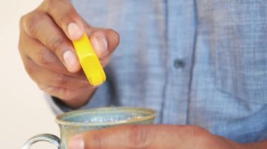 Genç adam çaya yapay tatlandırıcı koyuyor.