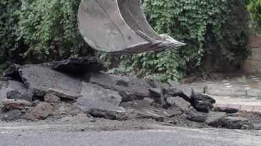 Devam eden yol onarım sürecinin bir parçası olarak bir kazıcı asfalt enkazını kaldırıyor